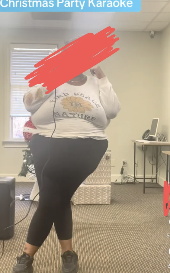 Person singing karaoke indoors, wearing casual covering  including leggings and a long-sleeve shirt. Nearby are a surface  and speaker