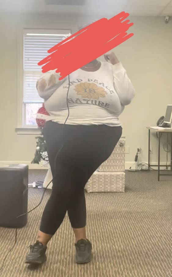 Person singing karaoke indoors, wearing casual clothing including leggings and a long-sleeve shirt. Nearby are a screen and speaker
