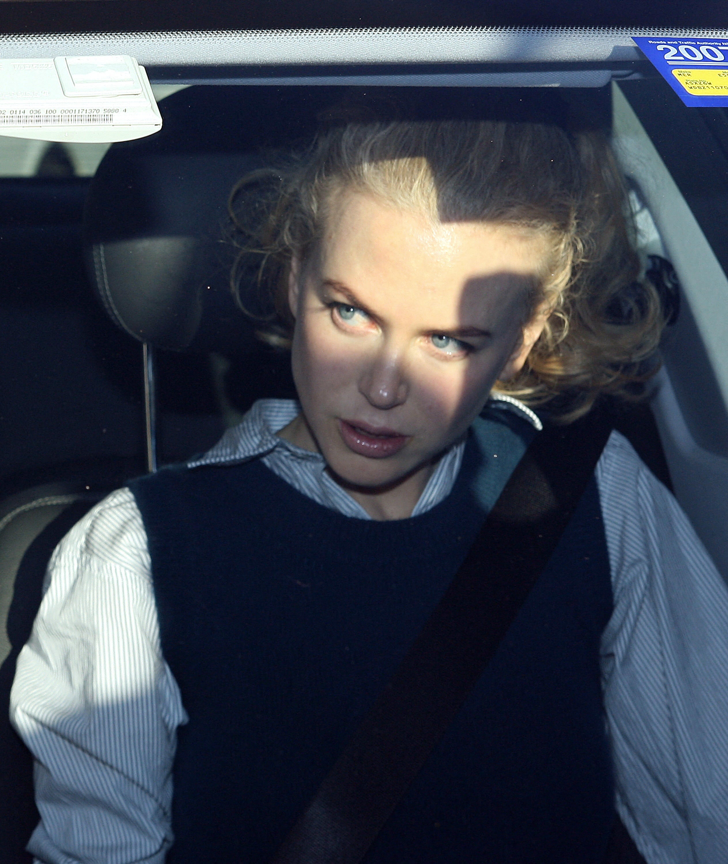 Nicole Kidman with curly hair is sitting in a car, wearing a striped shirt and a dark vest. They appear to be looking out the window