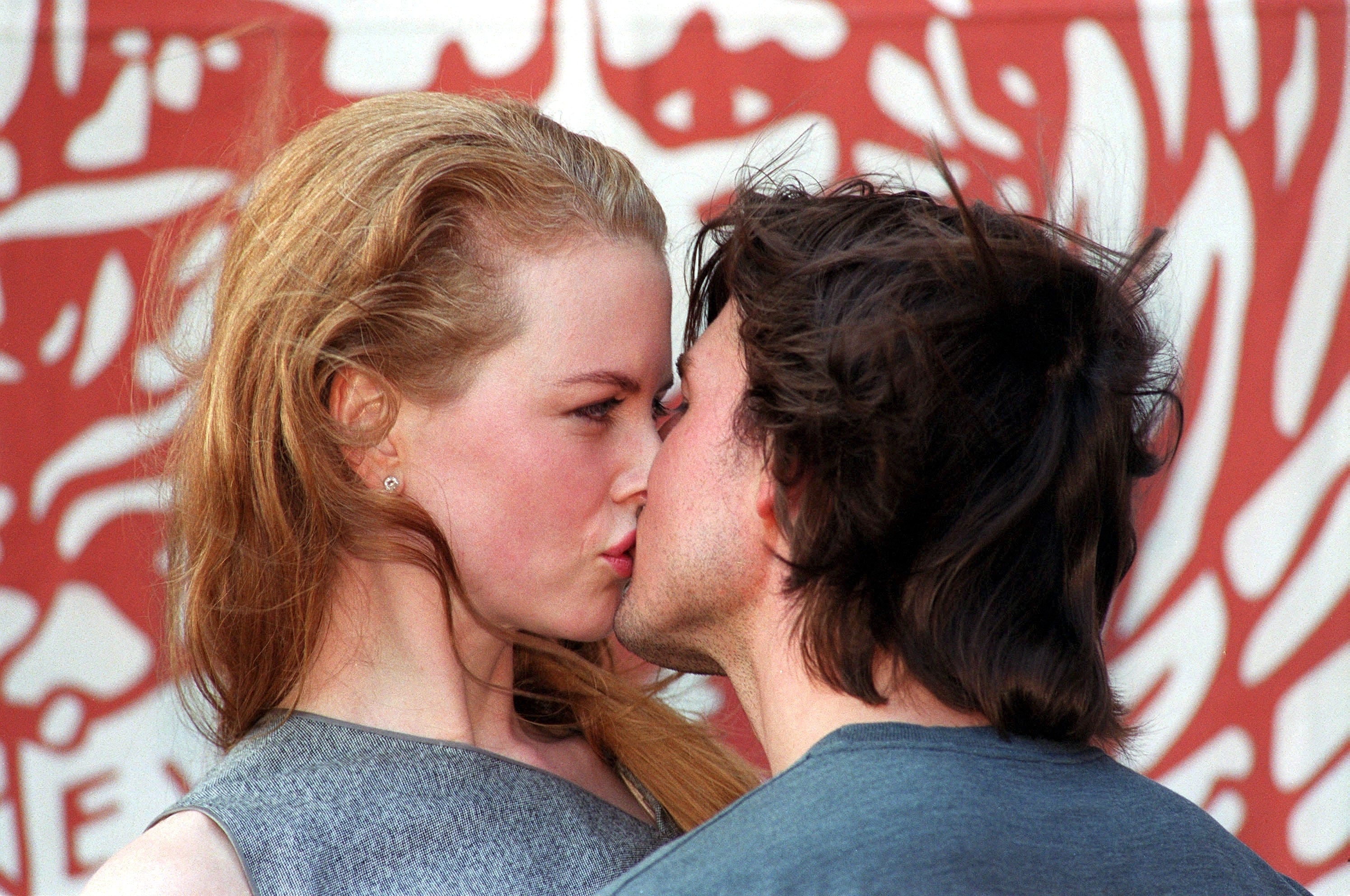 Nicole Kidman and Tom Cruise face each other closely, appearing to share a kiss. The background has a graphic design