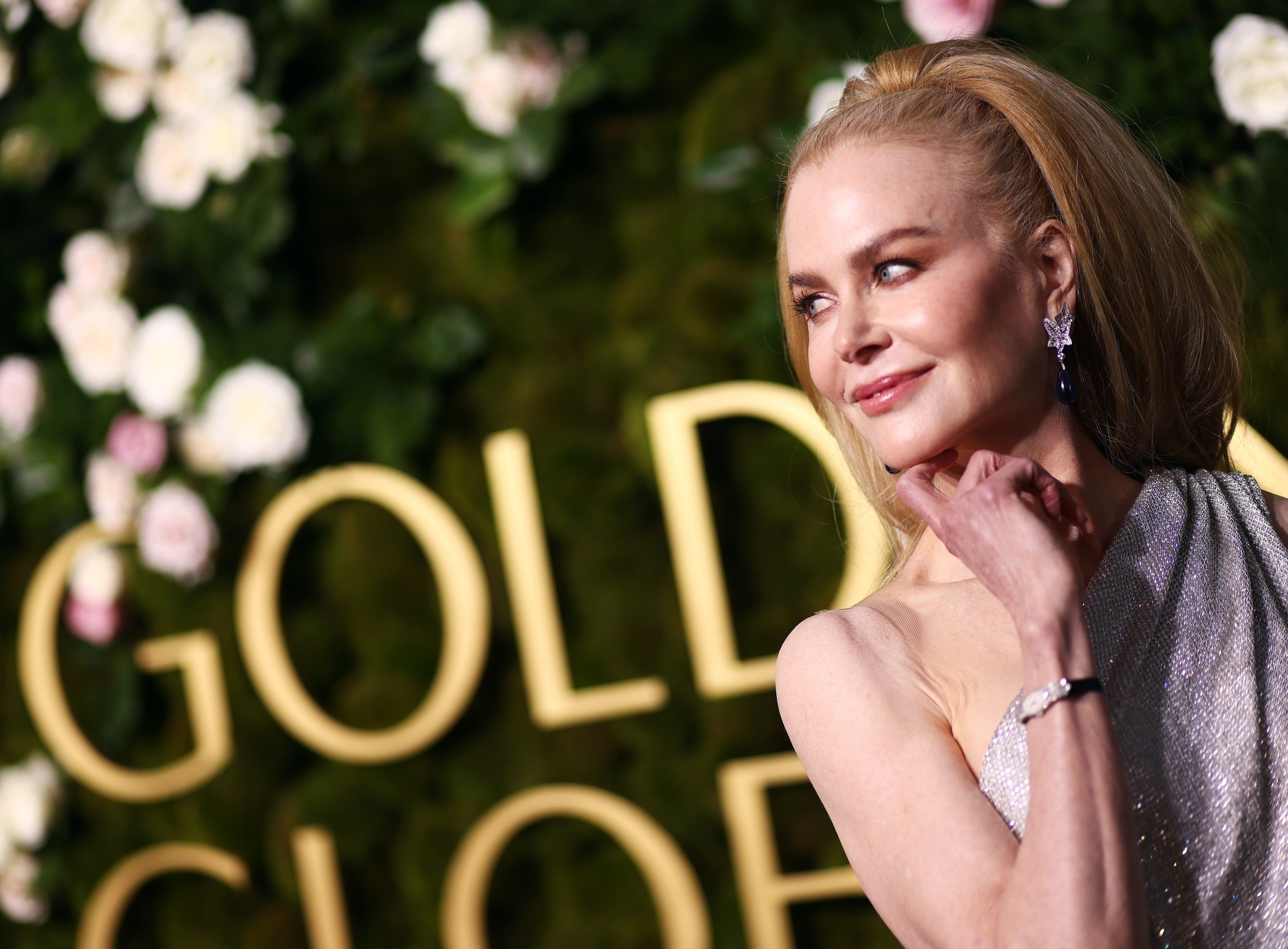 Nicole Kidman in elegant one-shoulder gown at an event, posing with a thoughtful expression and flowers in the background