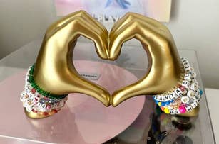 Gold hand sculpture forming a heart shape, adorned with colorful beaded bracelets
