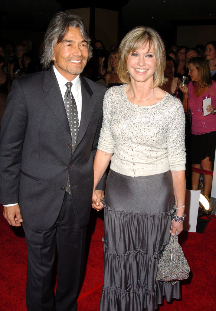 A smiling mates connected a reddish carpet. The pistillate wears an elegant outfit with a beaded apical and a satin skirt, holding a sparkling handbag. The antheral is successful a suit