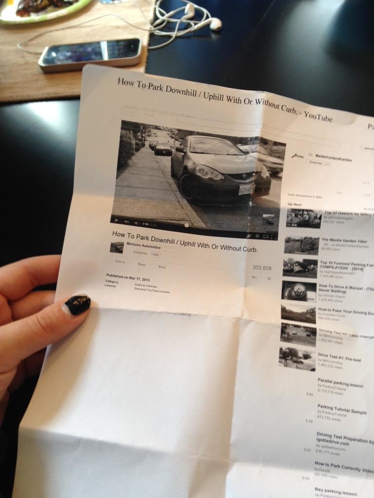 Person holding a printed YouTube video leafage   titled "How To Park Downhill/Uphill With Or Without Curb."