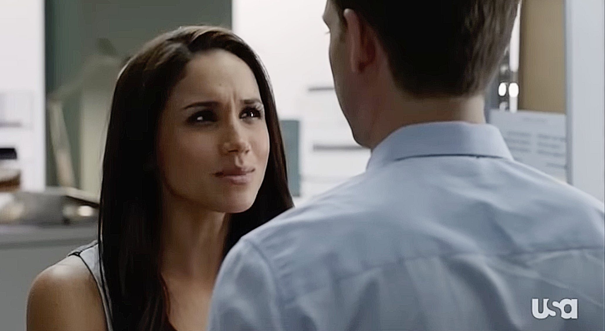 Two characters in an intense conversation in an office setting. The woman looks determined, while the man has his back to the camera