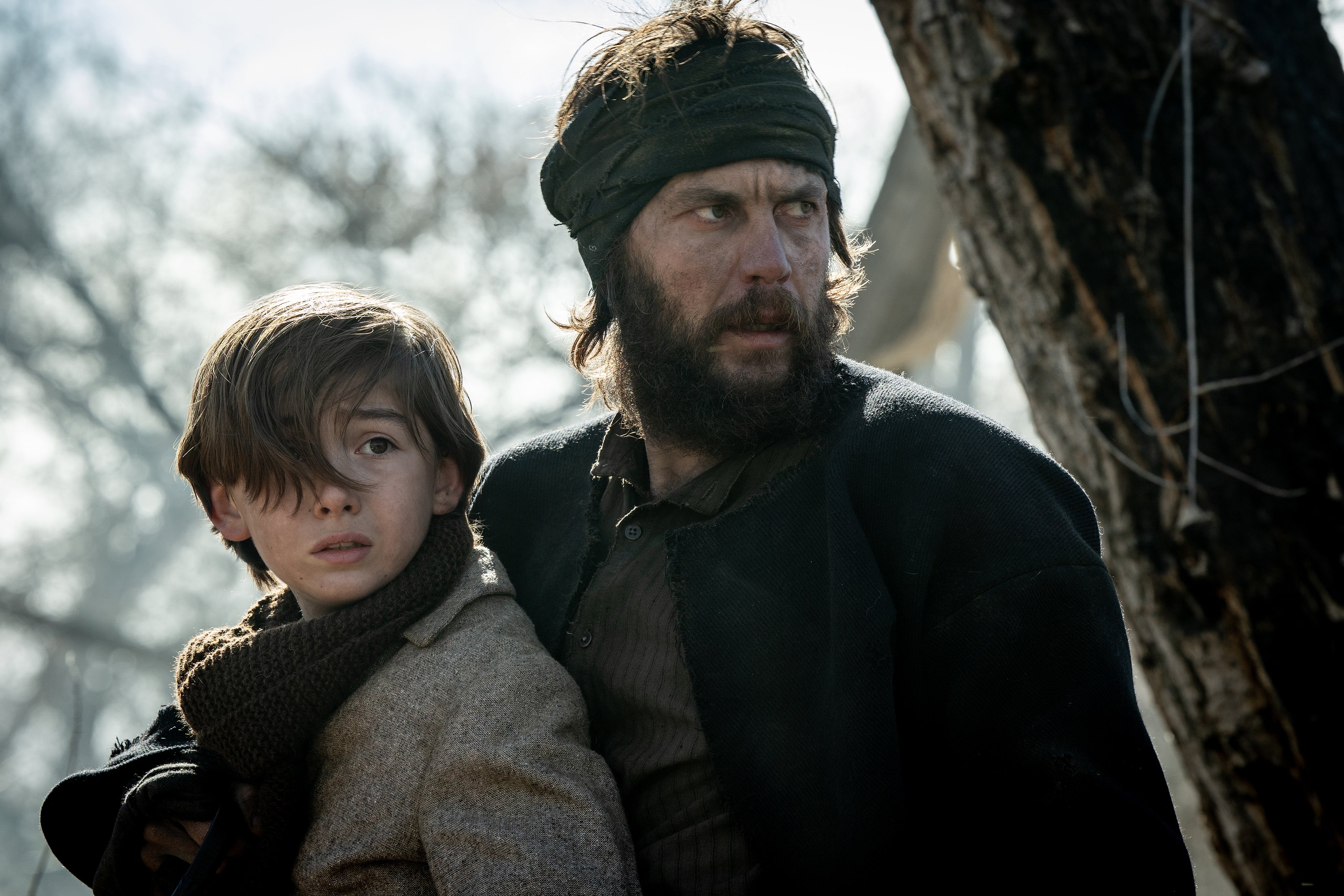 Scene from period drama with rugged man and child in outdoor setting, both looking intensely into the distance