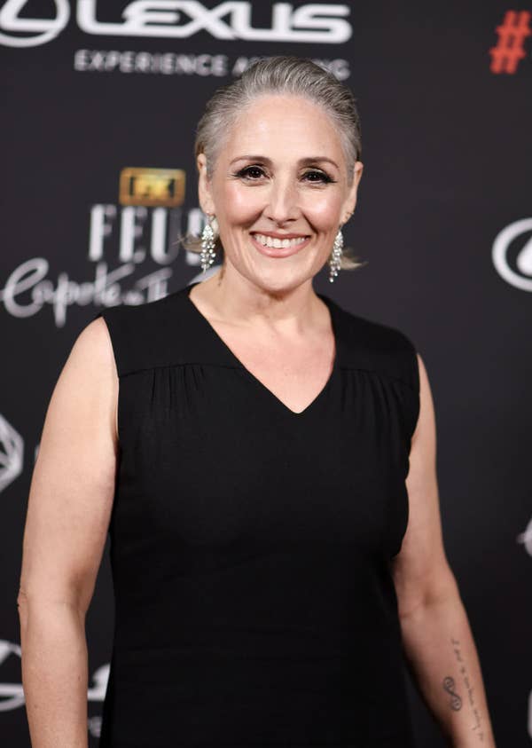Person in a black sleeveless dress on a red carpet, smiling