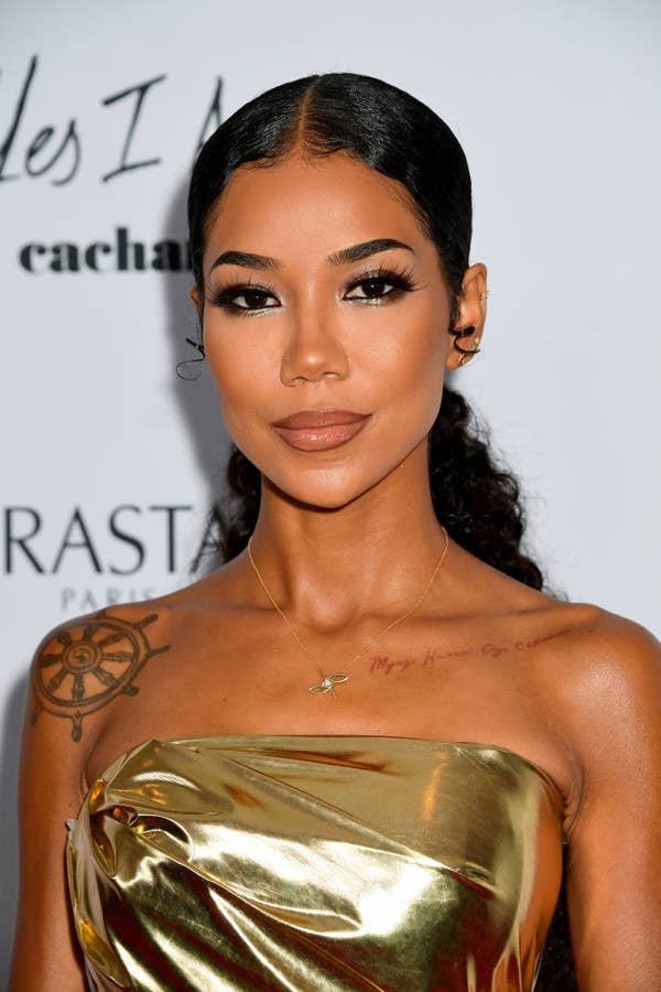 Person wearing a strapless metallic dress, with intricate makeup and visible tattoos, posing for a photo at an event