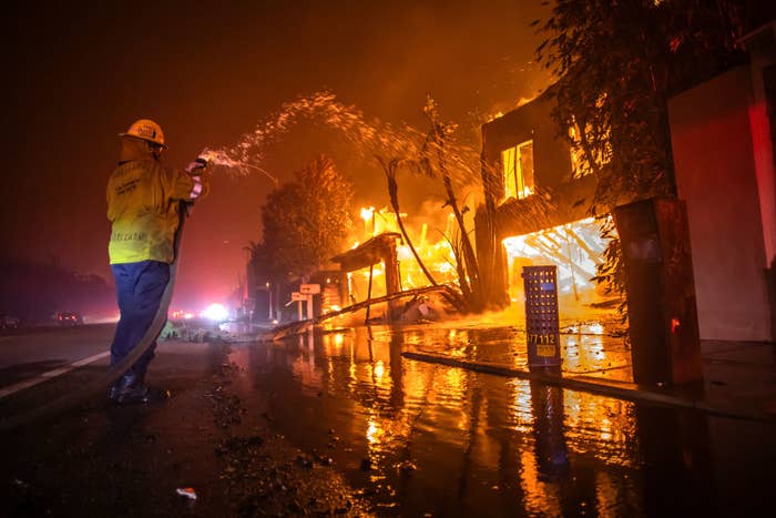Firefighter in uniform sprays water on a burning house during a nighttime fire scene. Emergency is ongoing