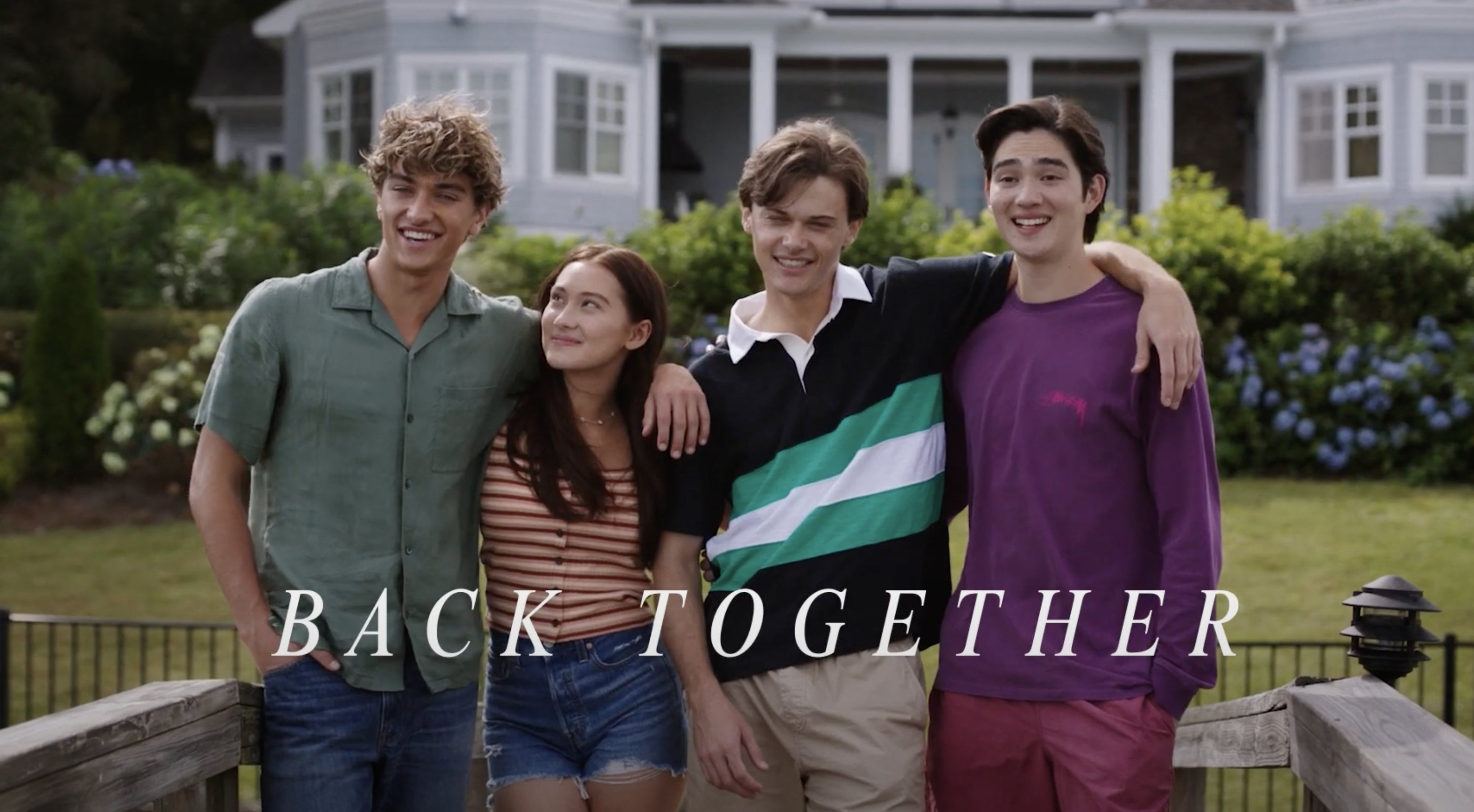 Four people with casual summer outfits stand together, smiling, in front of a house. The text reads "Back Together."