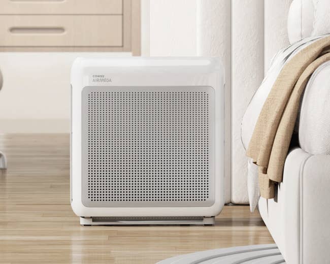 Air purifier placed on a wooden floor in a modern room setting with light-colored furniture in the background