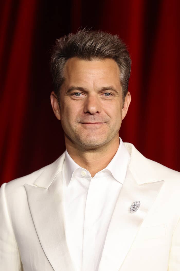 Person in tailored white suit jacket over white shirt, standing against a plain backdrop