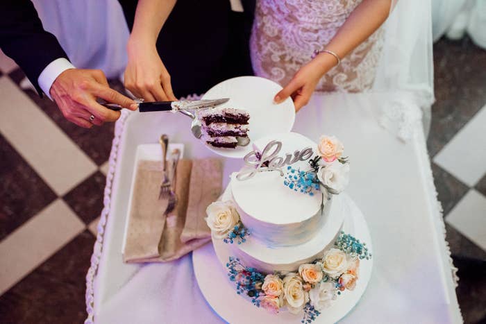 Couple cutting a wedding cake decorated with roses and a &quot;Love&quot; topper, symbolizing a romantic celebration