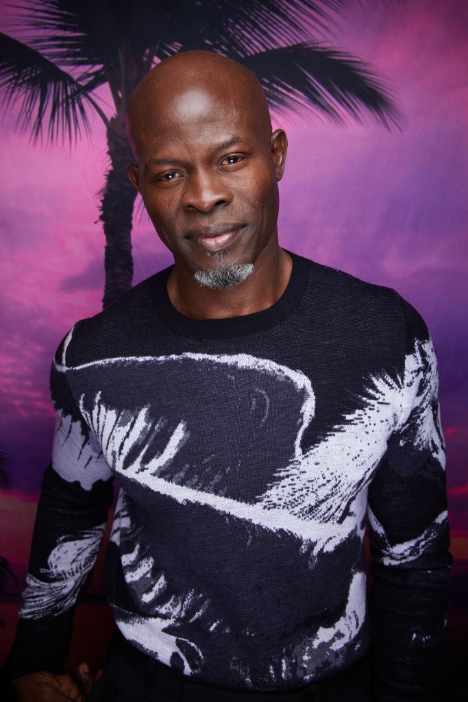 Man in patterned sweater poses in front of tropical backdrop
