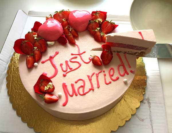Cake with &quot;Just married!&quot; written on top, decorated with strawberries and heart-shaped icing, with one slice being cut