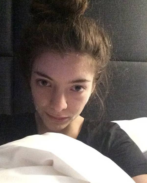 Person with hair in a bun, wearing a black top, wrapped in a white blanket, looking directly at the camera