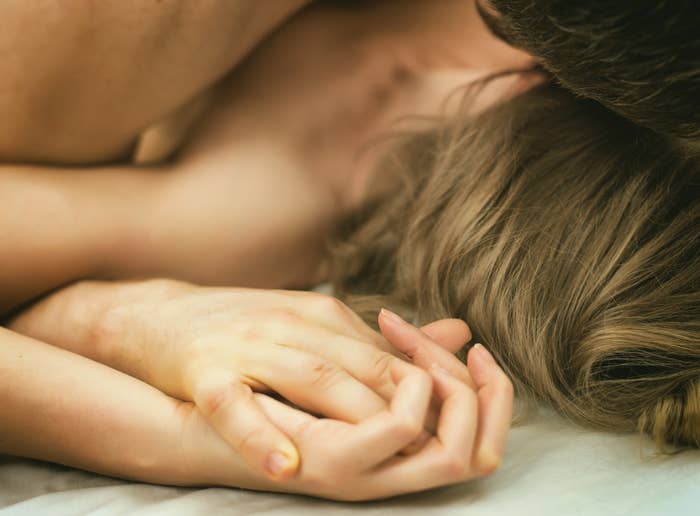 Two people lying closely together with their hands intertwined, conveying intimacy and connection