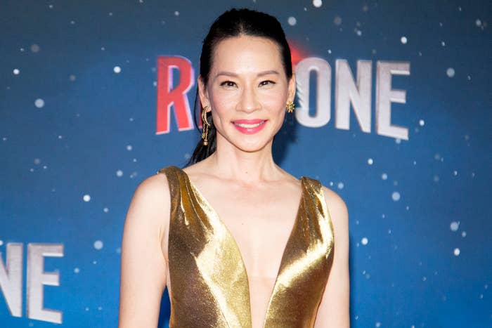 Lucy Liu on a red carpet in a stylish gold dress, smiling