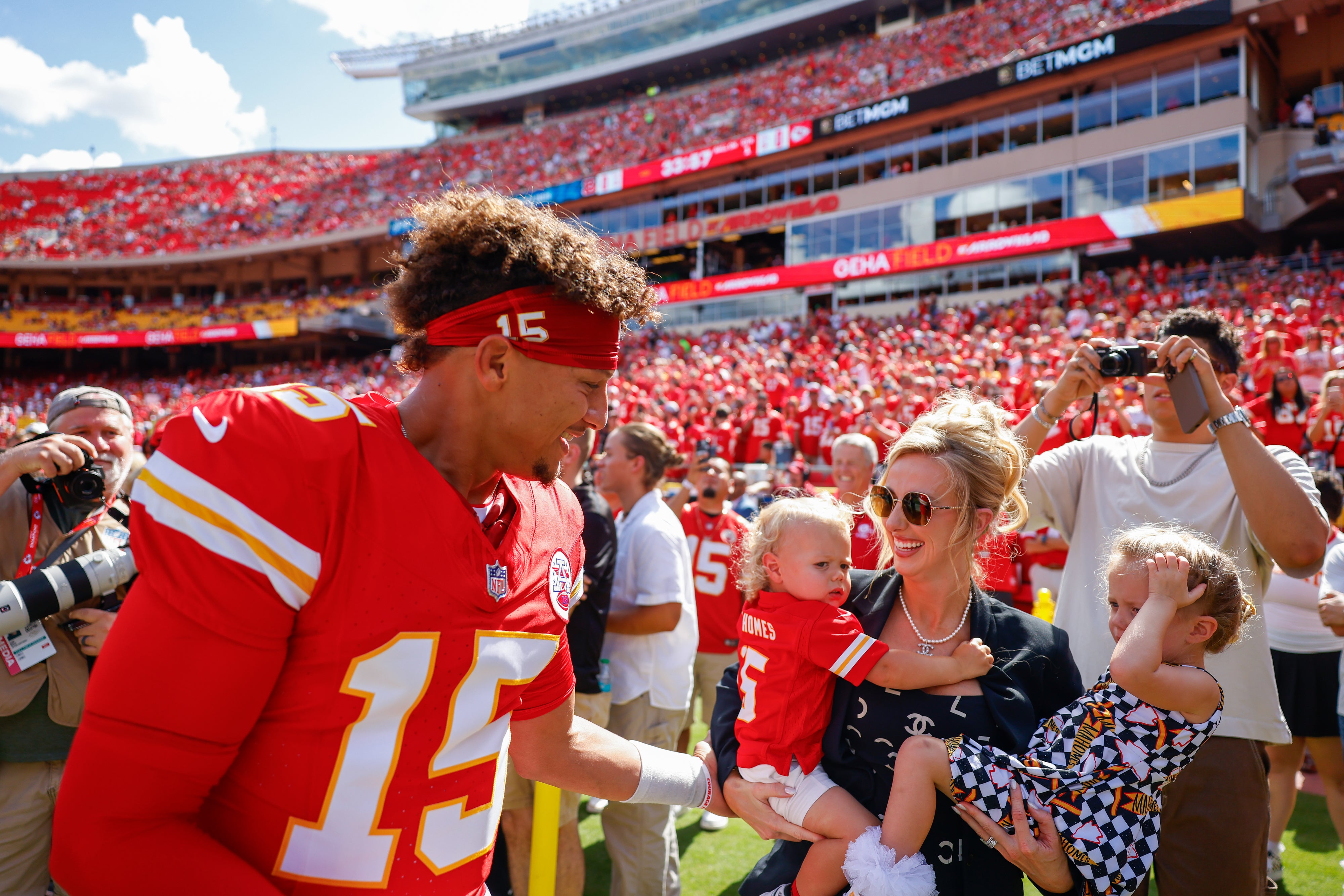 Football player in jersey number 15 greets a woman holding two young children at a stadium. The family appears happy and engaging with fans