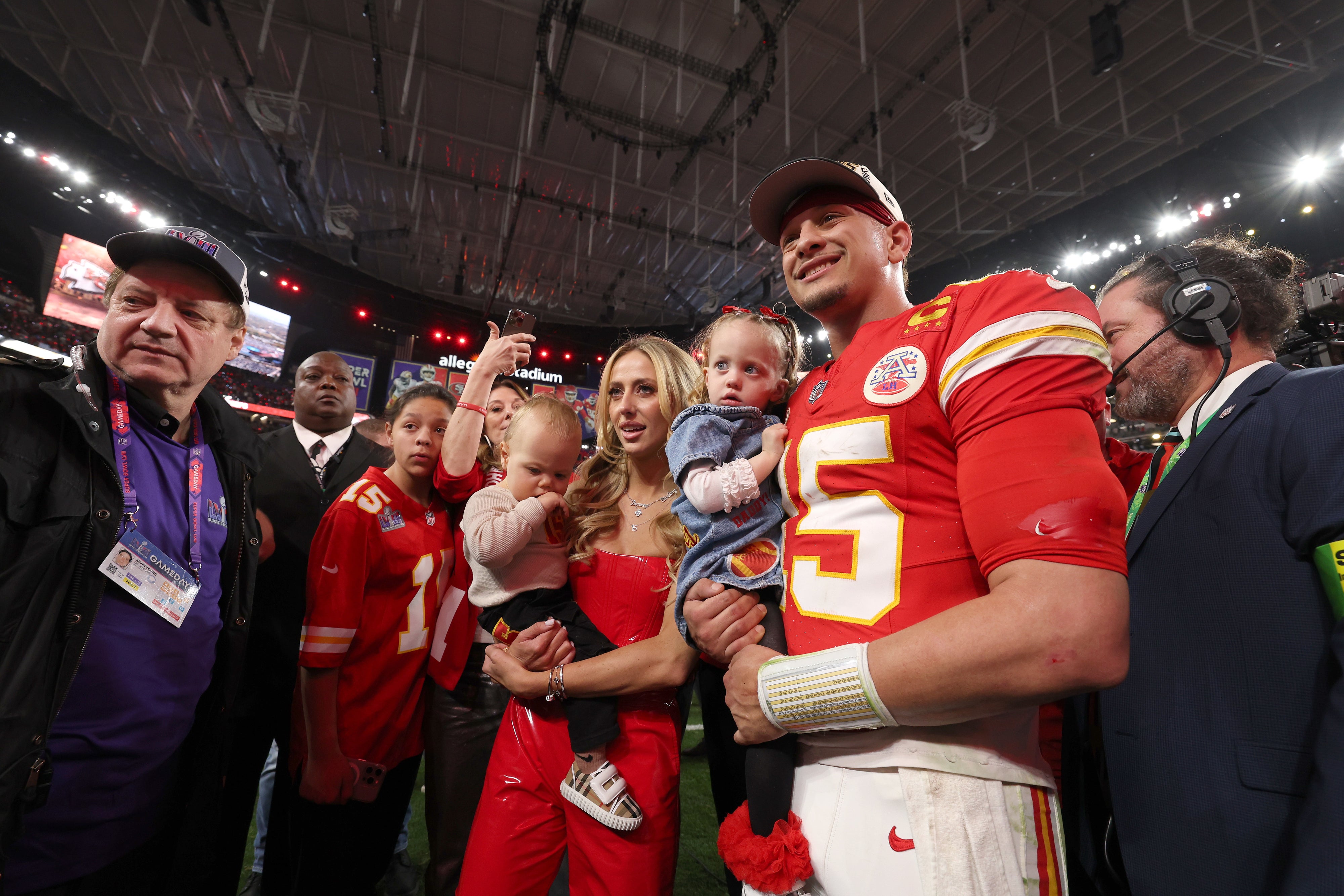 A football player in uniform poses with family and friends on the field after a game. The group appears happy and celebratory