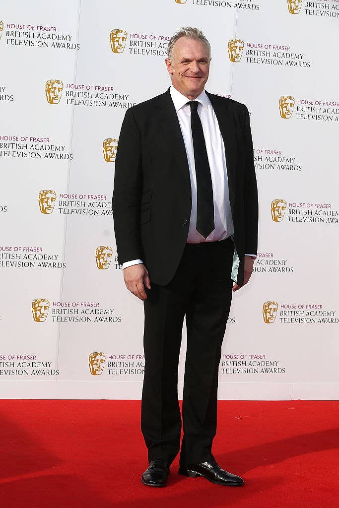 Greg in a formal suit stands on a red carpet at an awards event, smiling. Background shows event branding