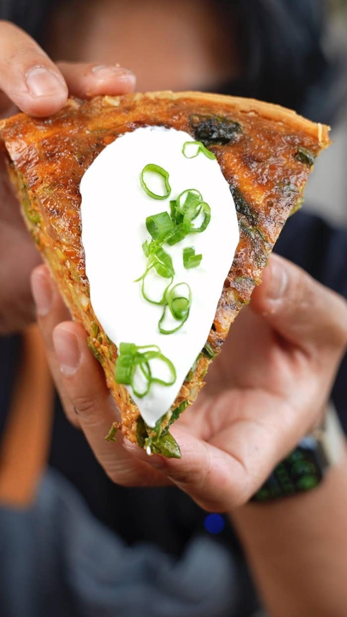 Slice of savory pie topped with sour cream and sliced green onions, held in hands
