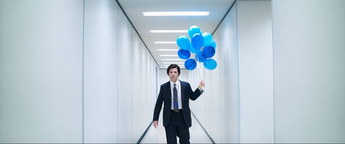 Person in a suit walking down a hallway holding a bunch of blue balloons