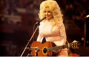 Dolly Parton performs on stage, wearing a sparkling dress and playing a guitar