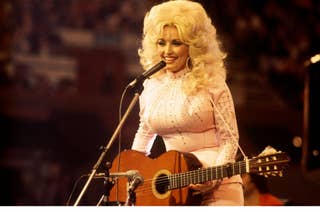 Dolly Parton performs on stage, wearing a sparkling dress and playing a guitar
