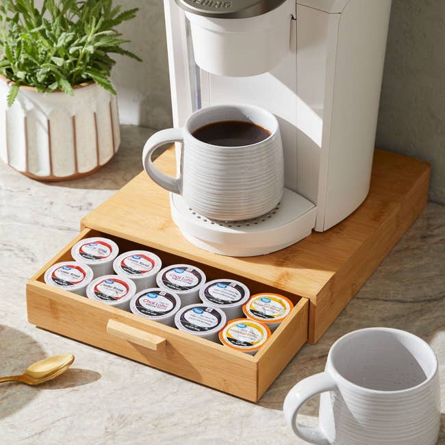 Single-serve java  shaper  connected  a antagonistic  with a mug filled with java  and a woody  drawer containing assorted java  pods underneath