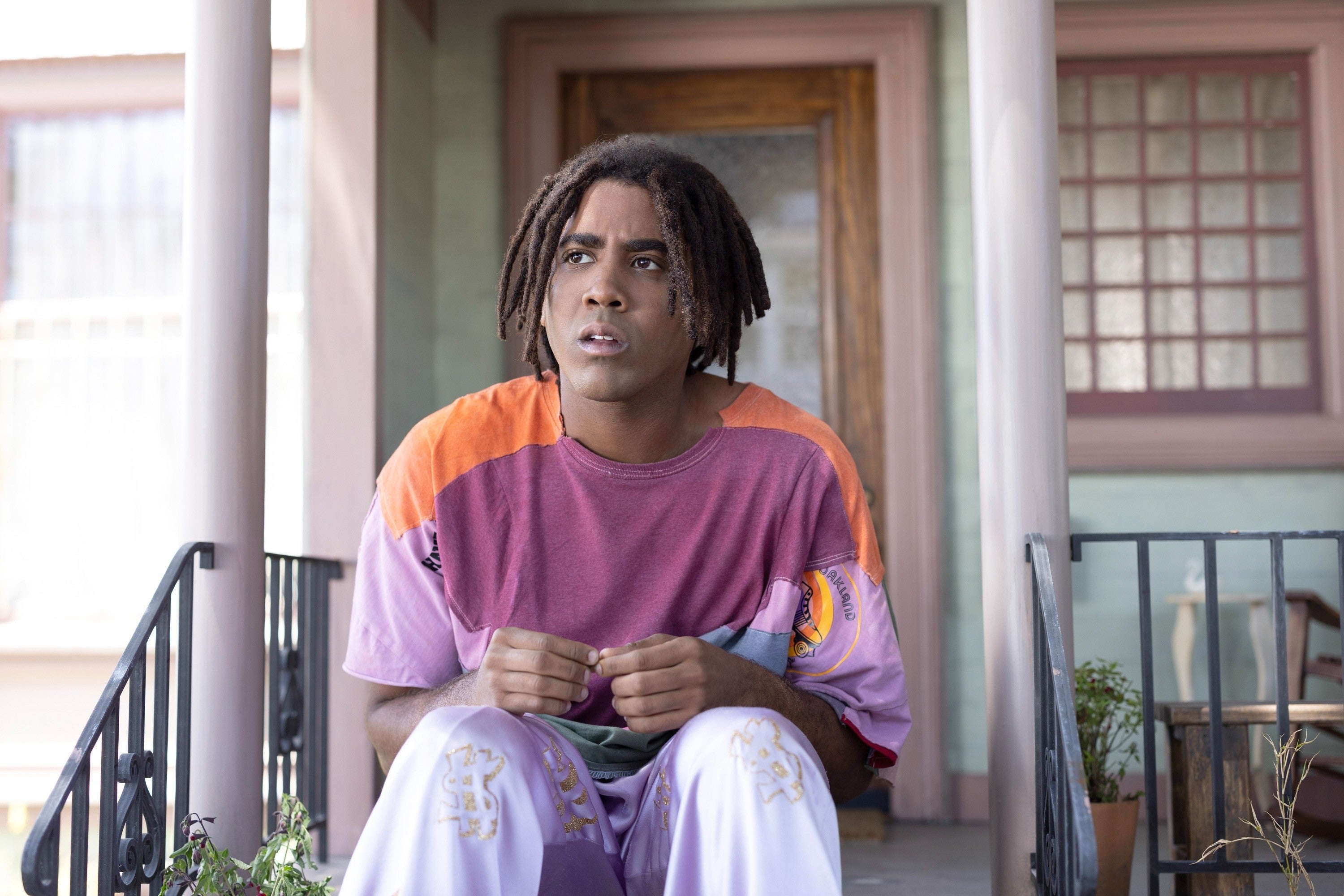Person sitting on porch steps, wearing a relaxed, casual t-shirt and pants, looking thoughtful