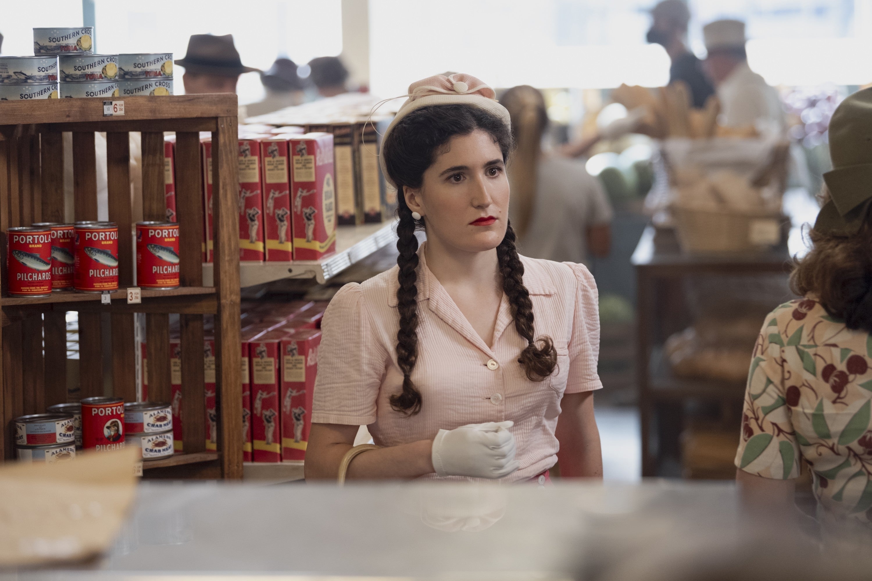 A woman with pigtails in 1940s attire shops in a grocery store, surrounded by shelves of canned goods and other shoppers