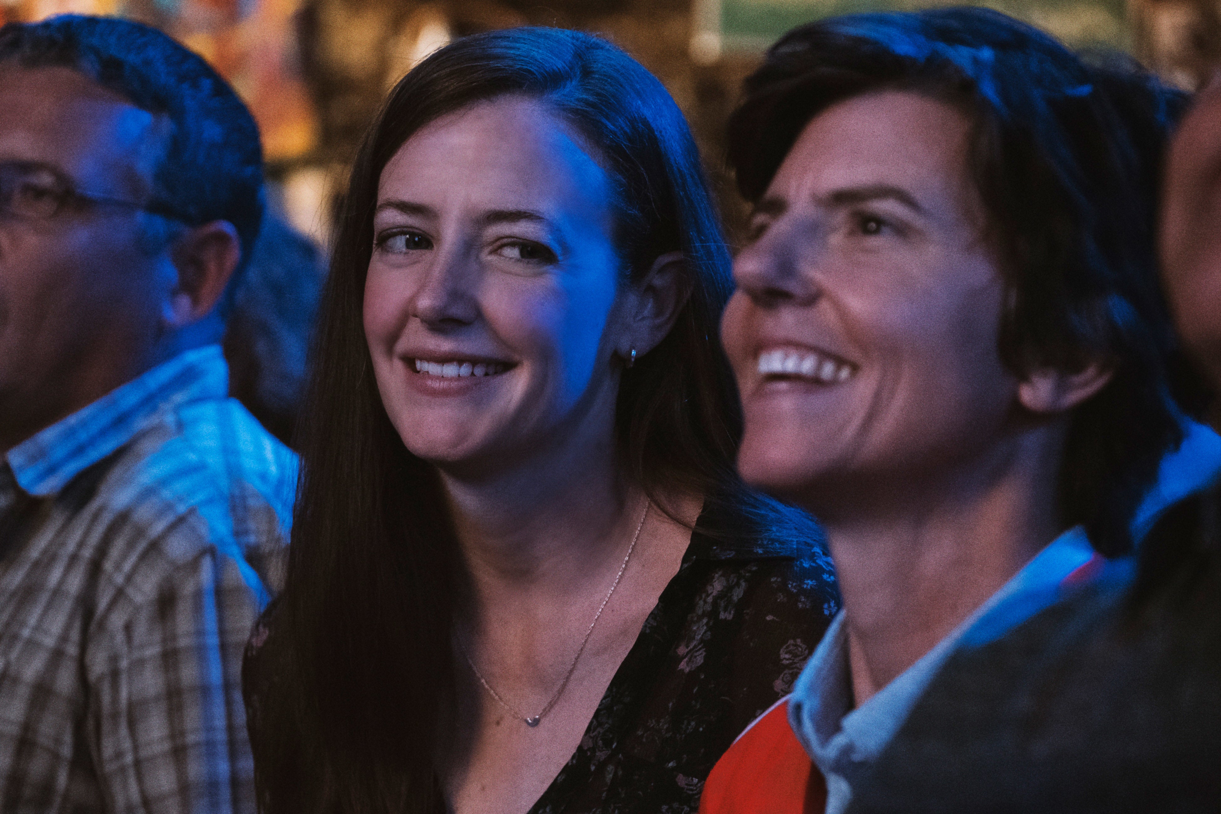 Two people smiling in an audience during an event. Both appear to be enjoying the moment