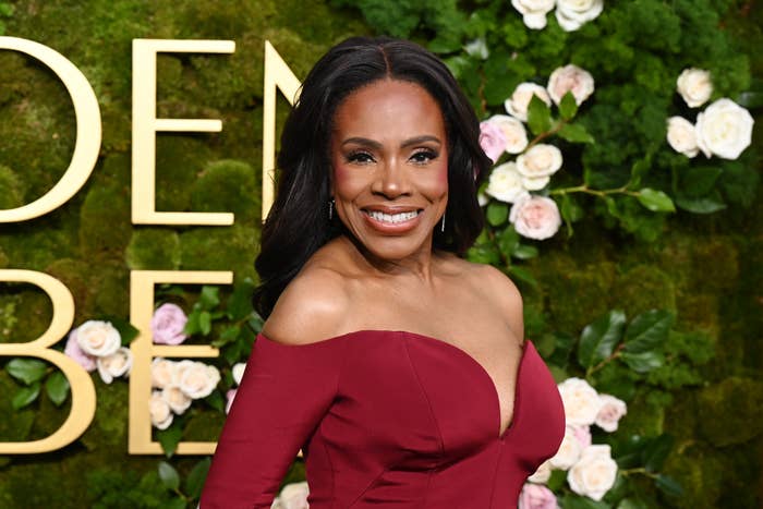 Sheryl Lee Ralph smiling in an off-shoulder gown with a floral backdrop, posing at an event