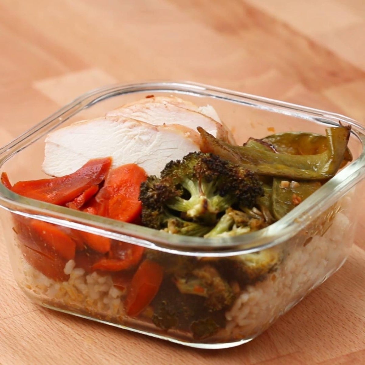 Meal prep container with sliced chicken, roasted broccoli, carrots, and brown rice