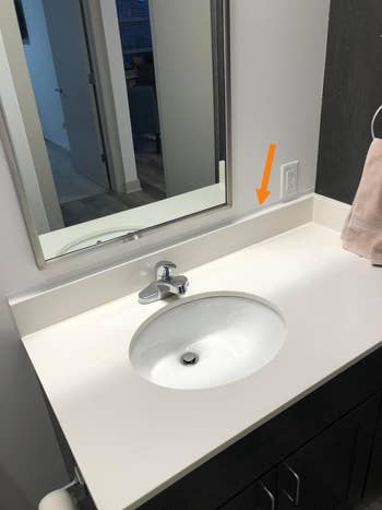 Modern bath  vanity with a achromatic  countertop, oval sink, and mirror; a beige towel hangs nearby