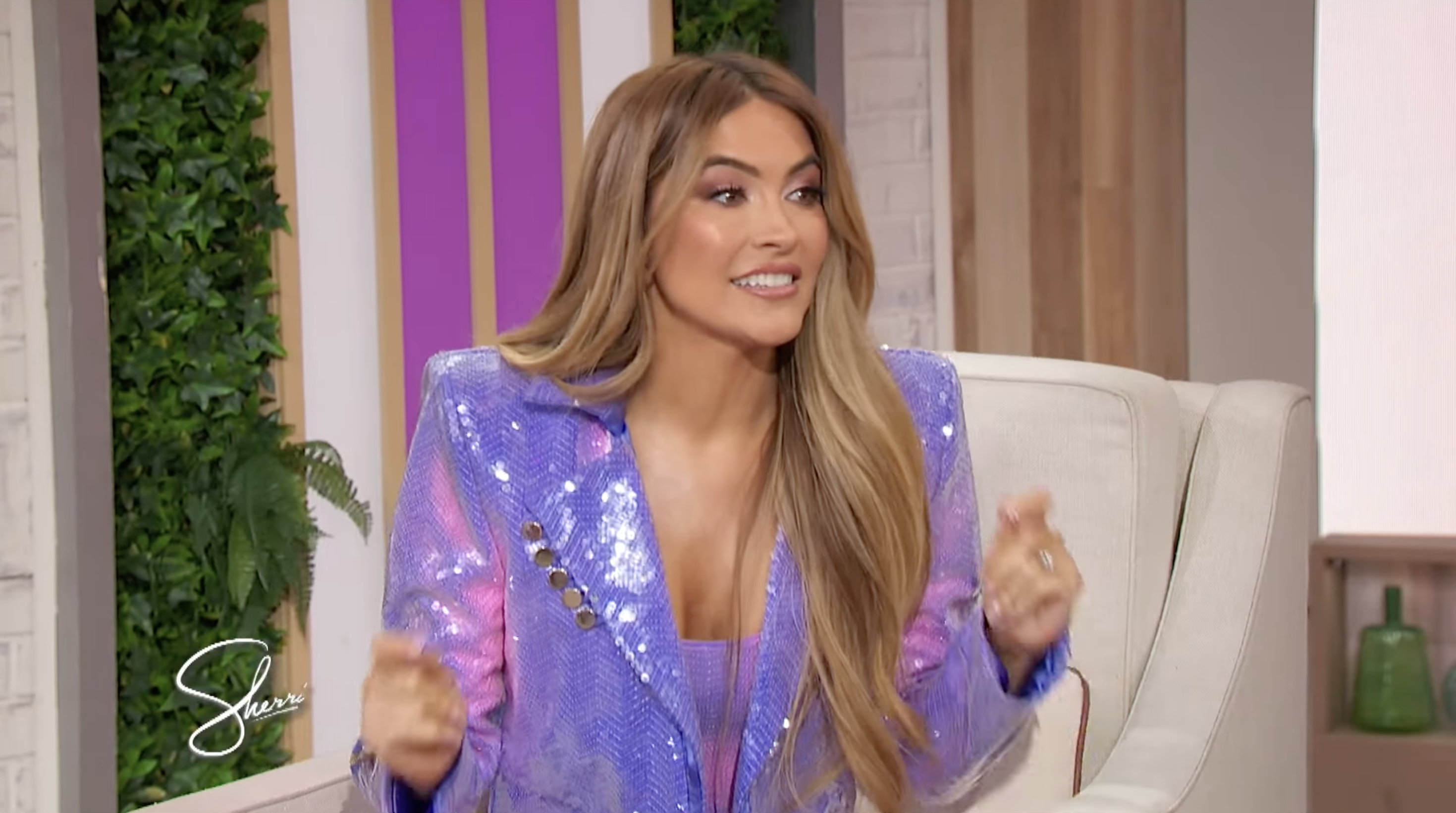 Person in shiny suit gesturing enthusiastically on a talk show set