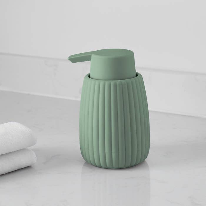 Ribbed soap dispenser with pump connected a bath antagonistic adjacent folded towels