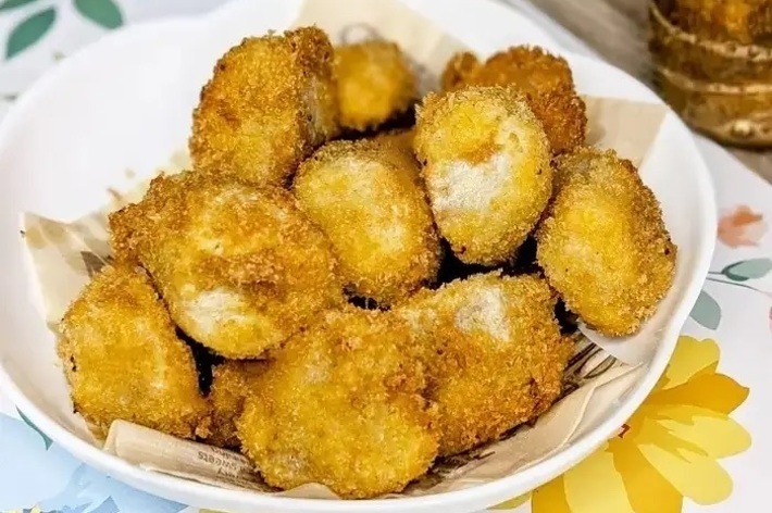 揚げた衣のカキフライが皿に盛られている。テーブルクロスには花柄があしらわれている。