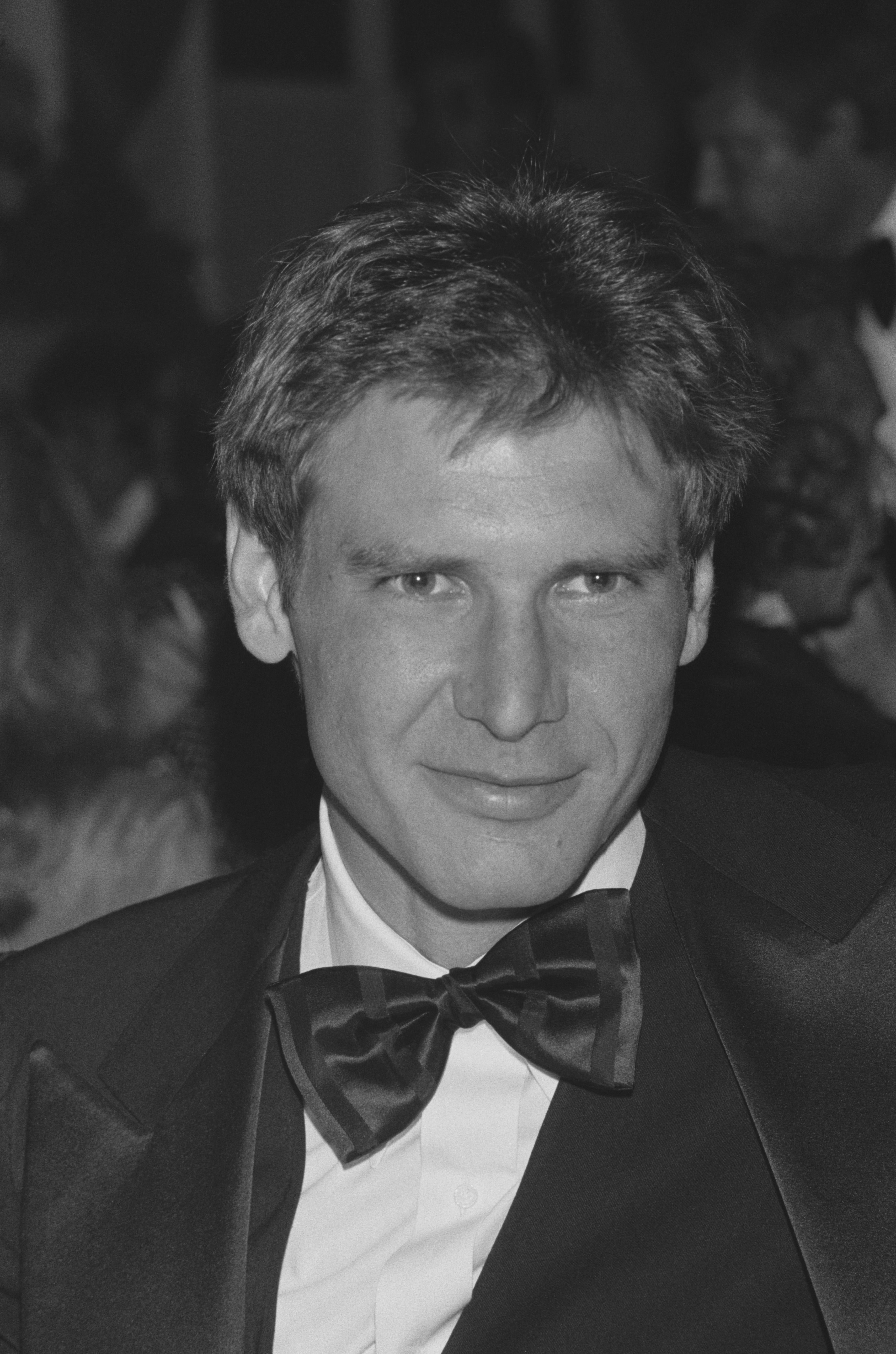 Young Harrison Ford in a tuxedo and bow tie, smiling at a formal event