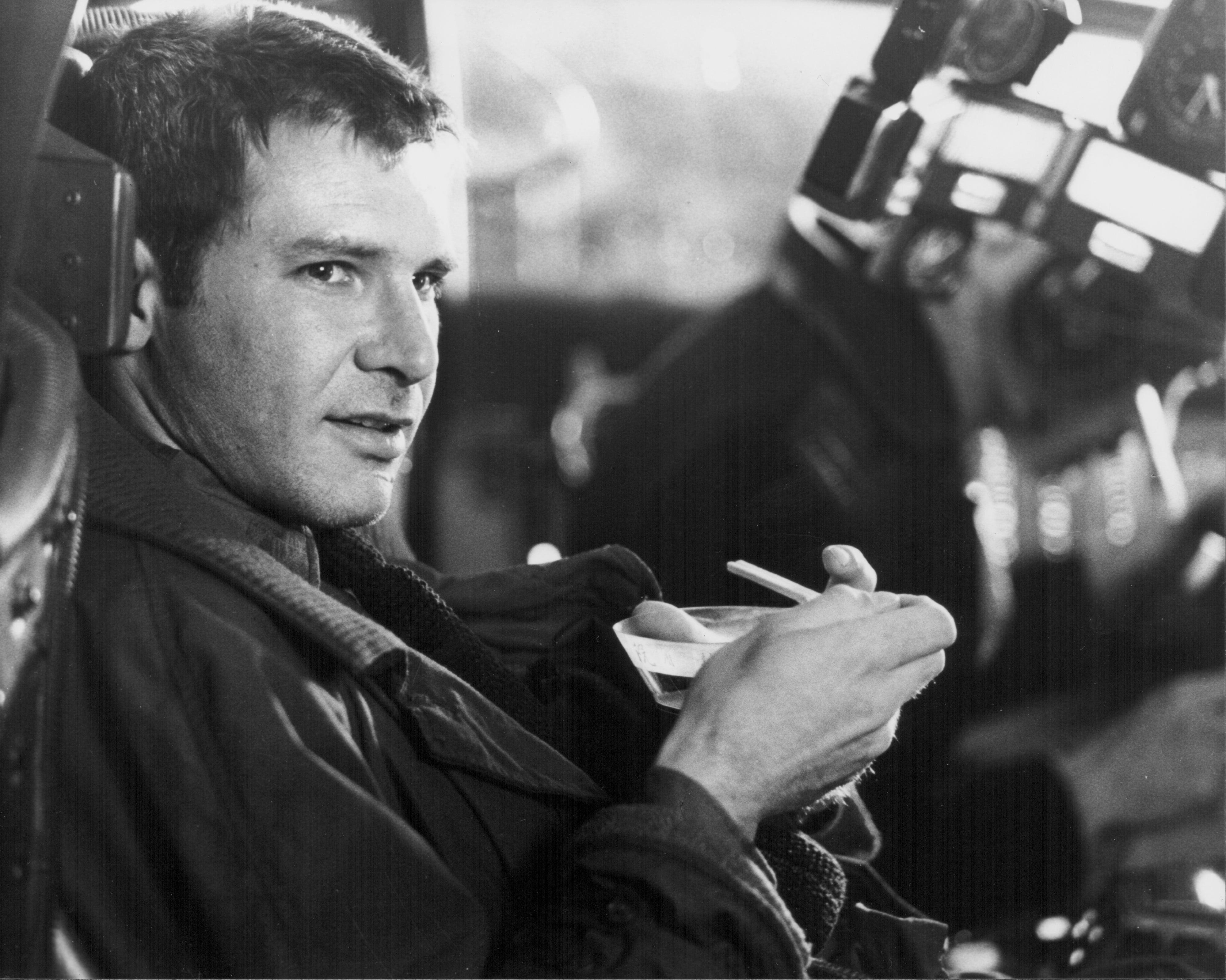 Harrison Ford on the set of "Blade Runner", seated, holding a bowl and spoon, looking sideways