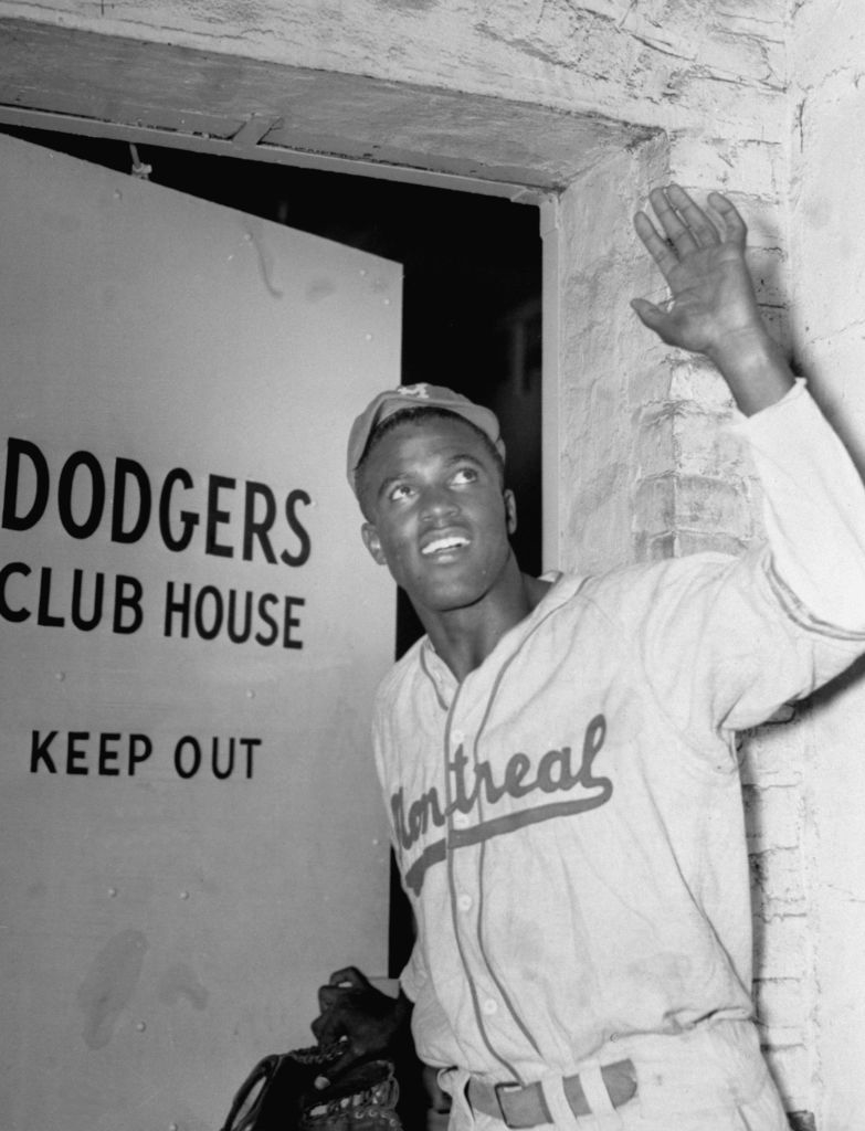 Person in baseball uniform waves, standing at entrance sign of Dodgers Clubhouse