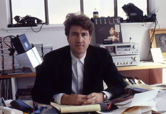 Person seated at a cluttered desk, surrounded by papers and office equipment, with records and a stereo system in the background