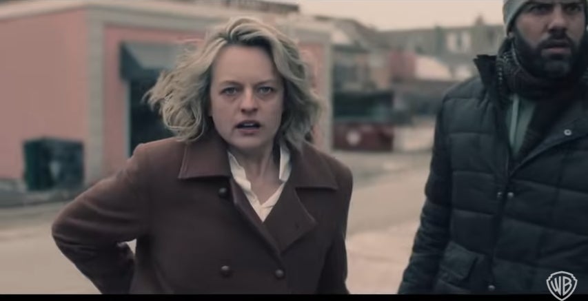 Two people stand tensely in a desolate street. The woman wears a brown coat; the man is dressed in a dark jacket and scarf. Scene from a TV show or movie
