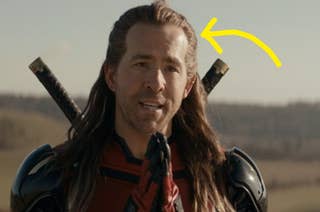 Person wearing armor with swords on their back, talking outdoors in a rural setting