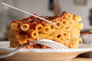 Close-up of baked ziti on a plate with a fork. An arrow points to a specific pasta noodle, emphasizing its texture and layers