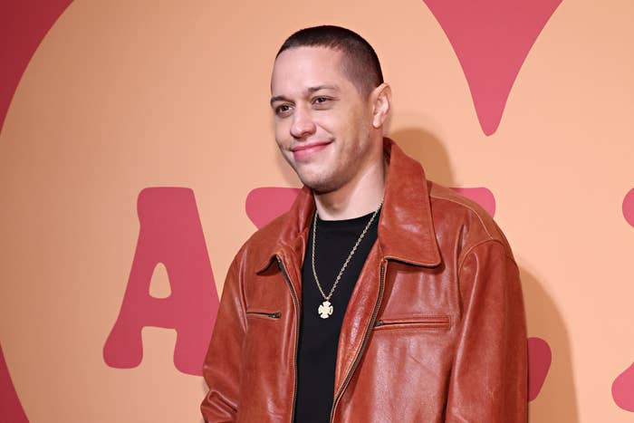 Person in a leather jacket smiles at an event with a large lettered backdrop