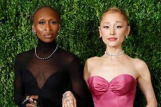 Ariana Grande and Cynthia Erivo in elegant dresses on a lush green backdrop: Cynthia in black with a sheer top, Ariana in a strapless pink gown, both with jewelry