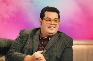 Person in a checkered blazer and orange glasses smiling, seated indoors