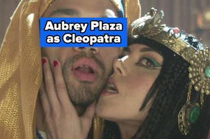 Two people in ancient Egyptian attire, one wearing a headdress and one with a jeweled headpiece, pose closely in an ornate setting